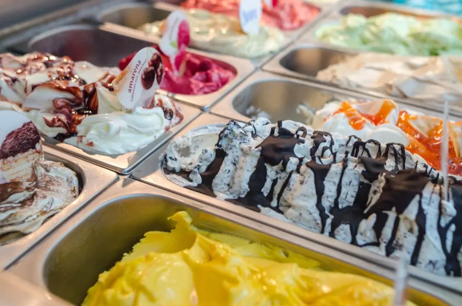 A gelato display case with rows of ice cream flavors including caramel, chocolate chip, and berry