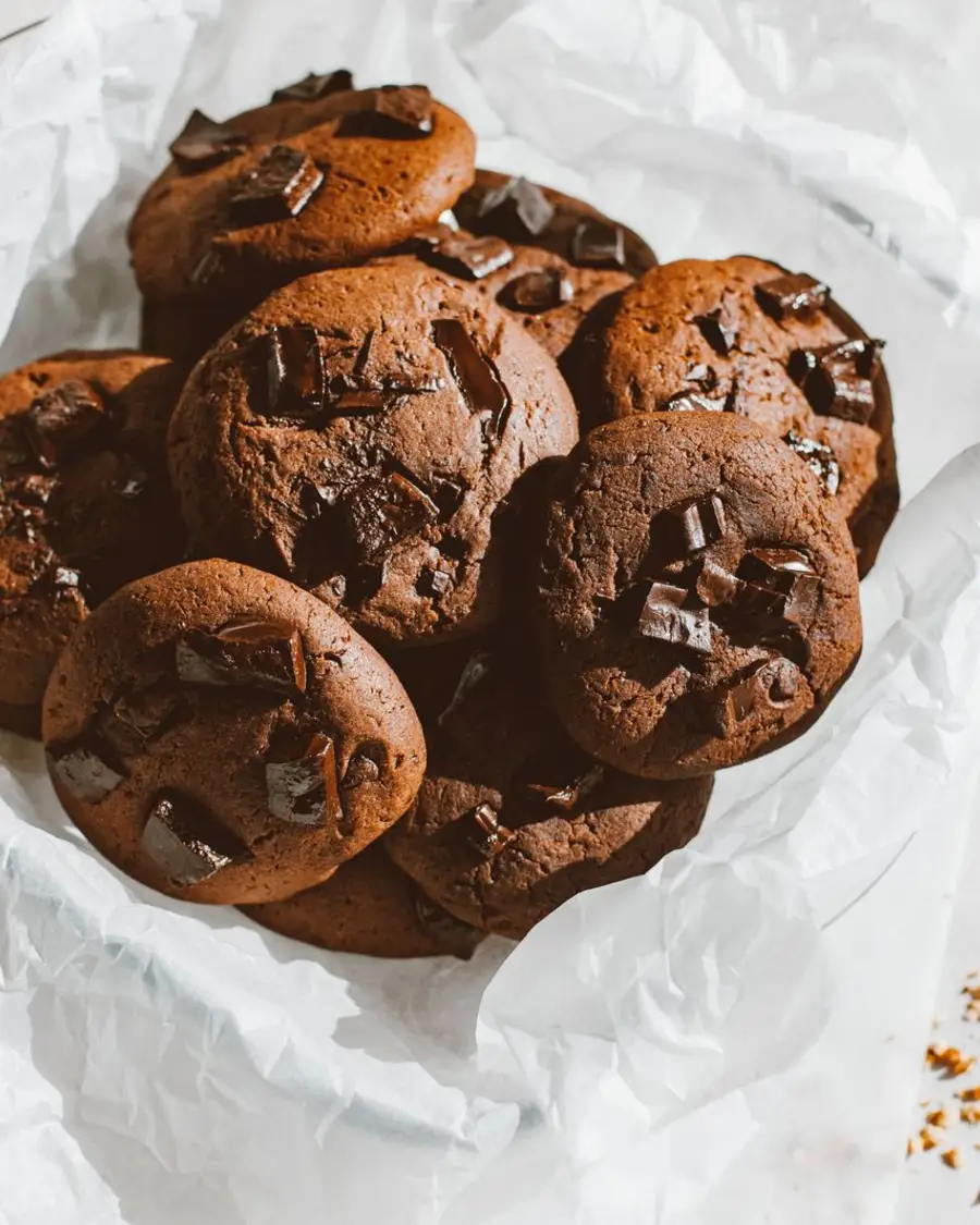 A pile of double chocolate chunk cookies fresh from the oven on parchment paper