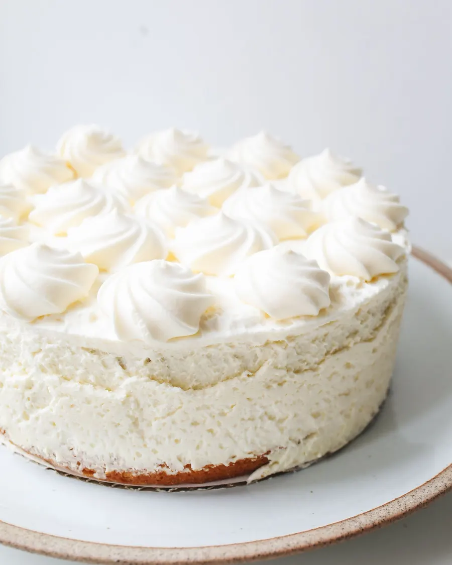 A frosted layer cake piped with billowy whipped-cream rosettes on a white plate