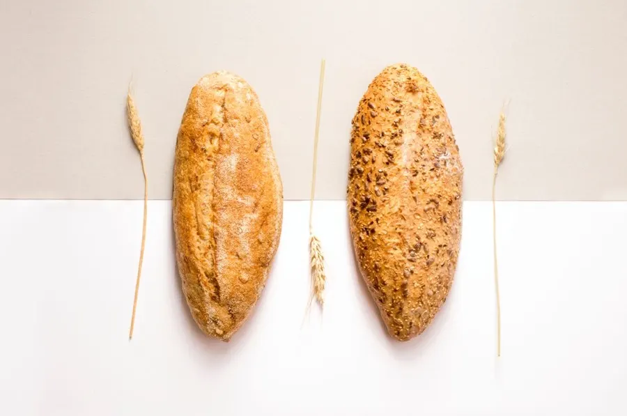 Two plain baked bread loaves on a calm neutral background, styled with wheat stalks