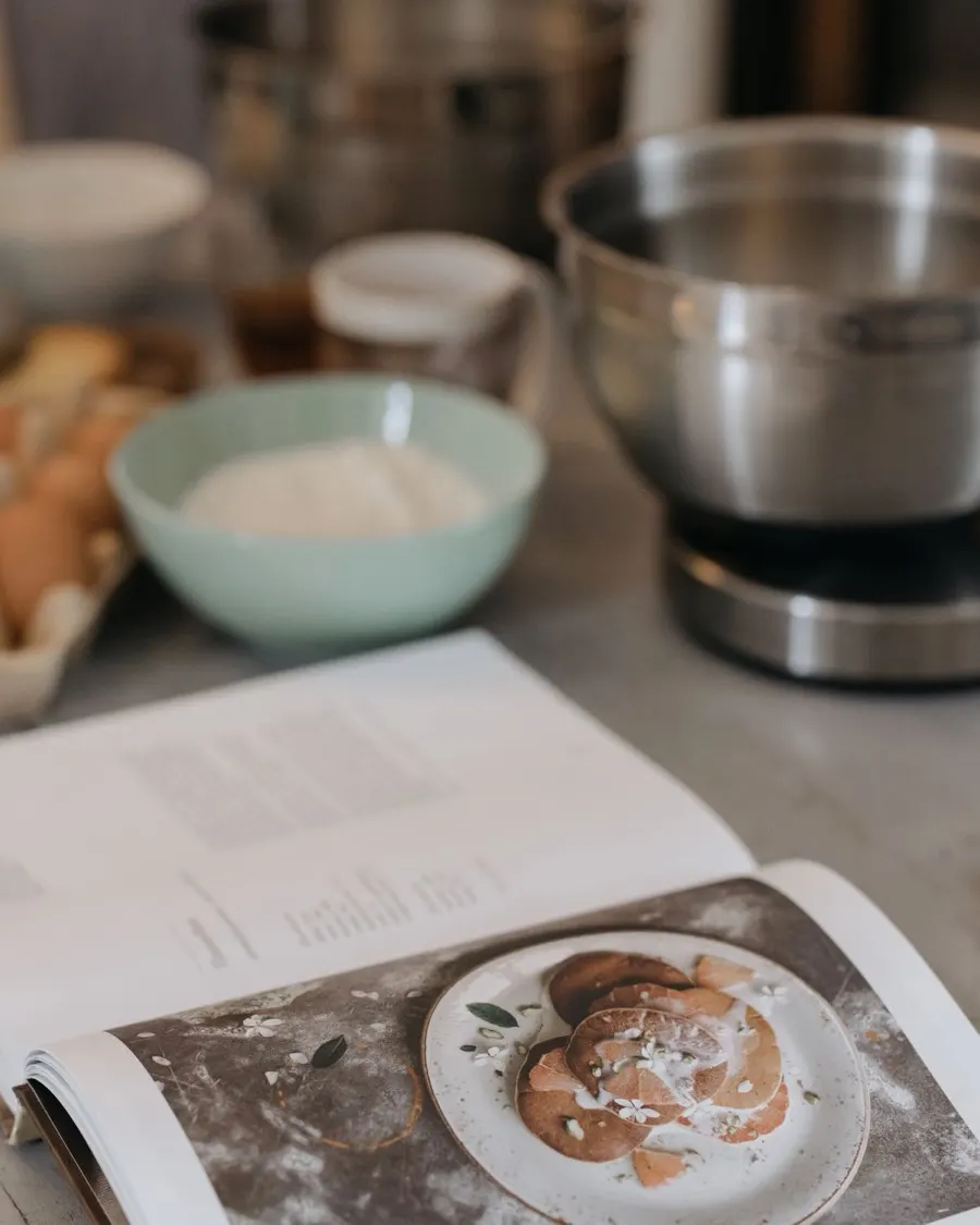 An open cookbook page beside mixing bowls and baking ingredients on a kitchen counter